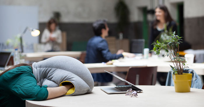 Women using the Ostrich Pillow to take a nap on a table