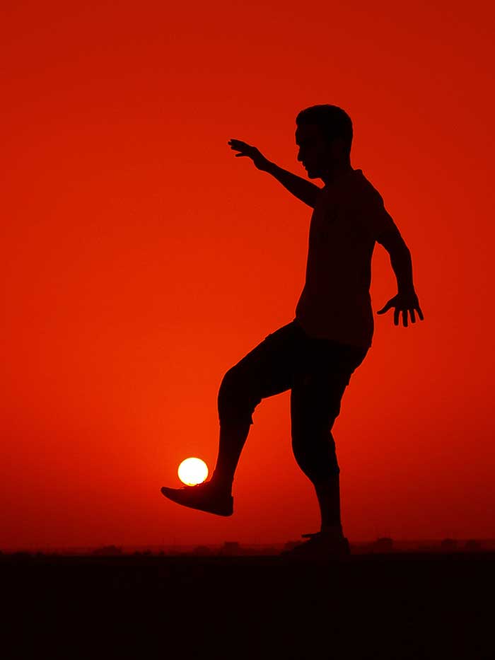 A guy playing soccer with the sun