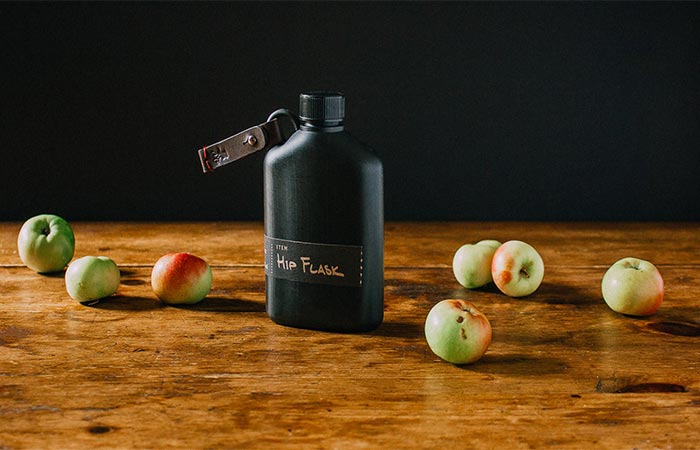 Black Bush Smarts Hip Flask On A Wooden Table With Apples Around It