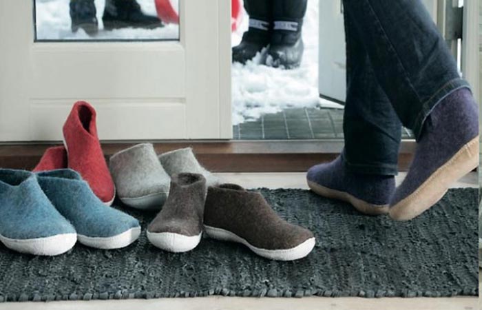 Glerups shoes in different colors piled up at the door step, and a person wearing a pair exiting through the door.