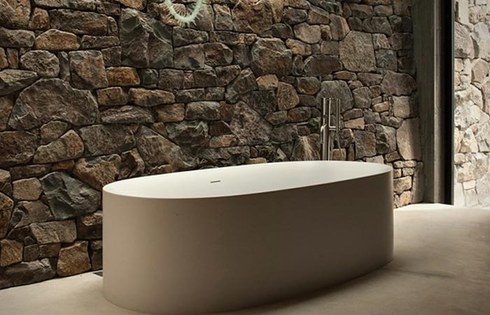 Seascape Retreat on a South Pacific Cove, the tub, covered, in front of a rocky wall, with an open door further.