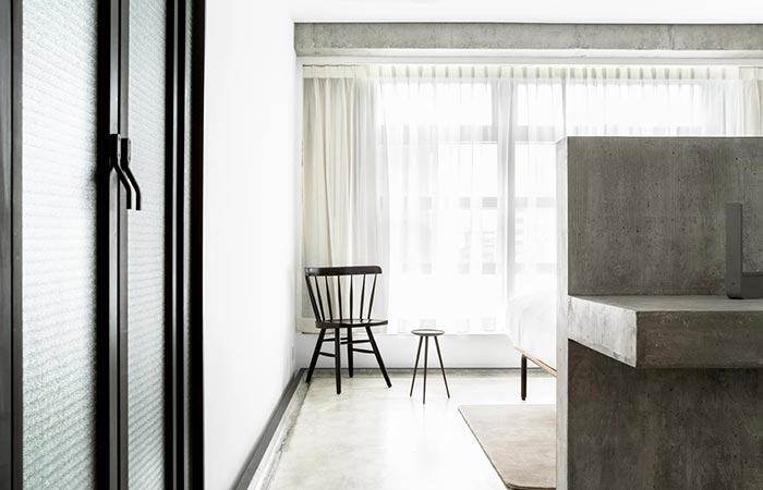 TUVE Boutique Hotel room interior, a glass door, a small concrete wall, and a chair in front of the window. 