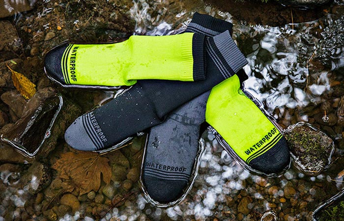 Showers Pass Waterproof Crew Socks, black/grey and neon yellow, lying on some rocks in a stream. 