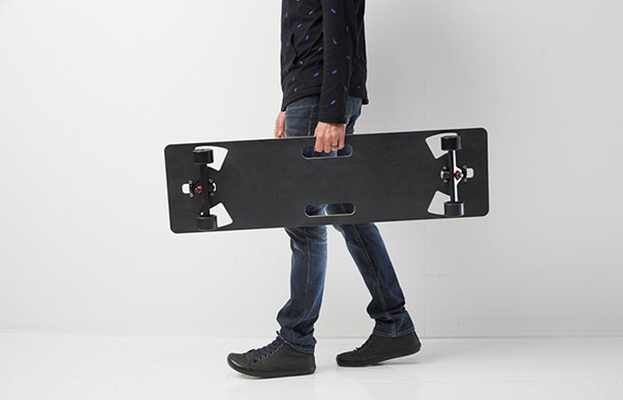 A man carrying the Lo-Ruiter Longboard, side view, in front of a white wall.