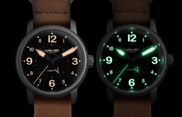 Lum Tec Combat B33 GMT watch with brown leather strap and white display and with black nylon strap and old radium tone luminescence, on a black background.