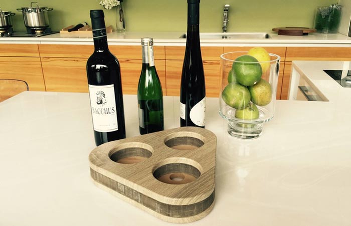 The Deck - Flexible Wine Holder, folded, on the kitchen counter with three different wine bottles and with a bowl of apples.