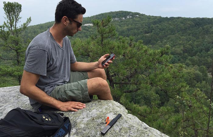 goTenna on a rock next to a guy while he's using his phone.