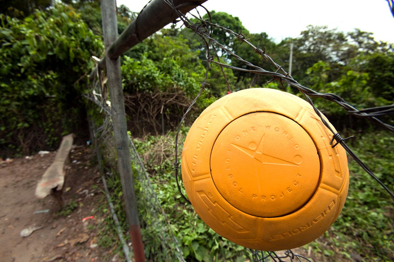 Yellow One World Futbol Soccer ball on a barb wire fence