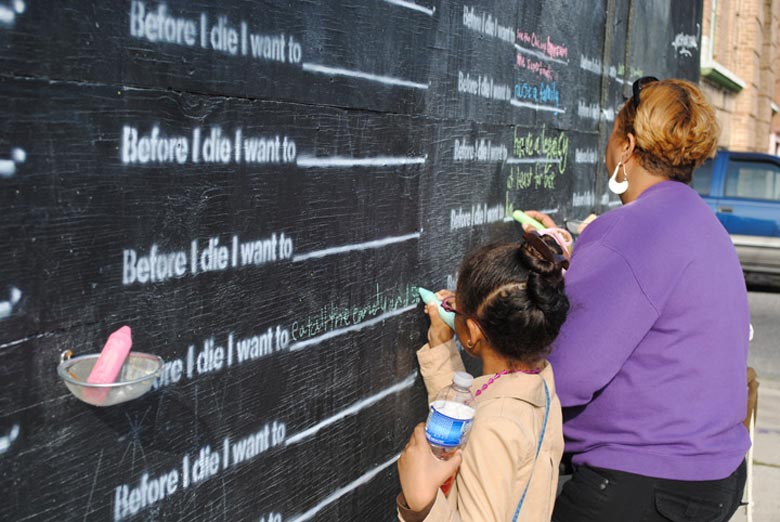 Little girl writing on the Before I Die wall by Candy Chang