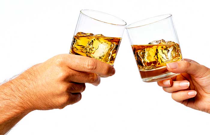 A man and a woman's hand with glasses of whiskey