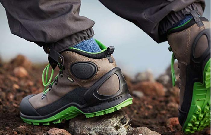 The Biom Terrain Hiking Boots green/gray, worn, on a rocky terrain.