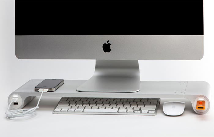 A desk with an aluminum Quriky Space Bar, a computer monitor and phone on deck, and a keyboard and mouse underneath.