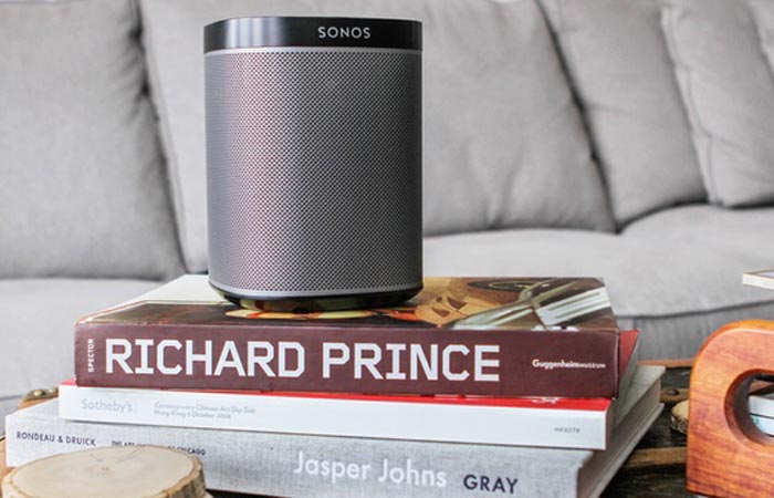 Sonos speaker on a pile of books with a sofa in the background.