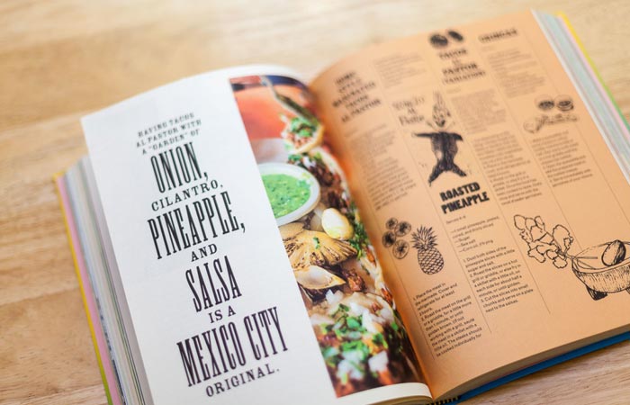 Tacopedia book, open, on a wooden table, two pages with text, illustrations and photos.