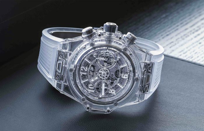 Hublot Big Bang UNICCO Sapphire with transparent strap, laid on the side, on a grey surface.