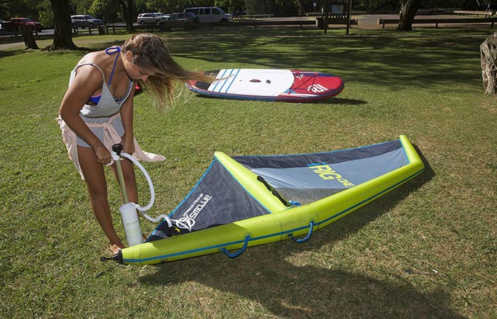 A woman inflating the iRig One with a pump, standing bent down on grass, with a board in the background.