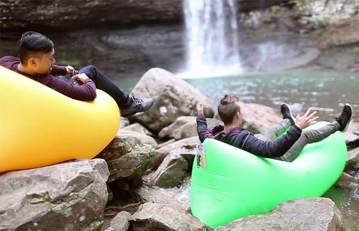 Two people sitting on green and yellow windpouches on rocks close to a waterfall