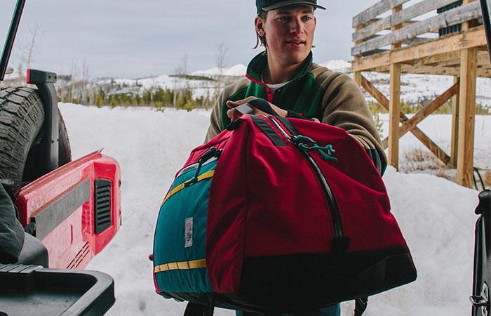 A Guy Putting Red Topo Designs Mountain Duffel In The Car
