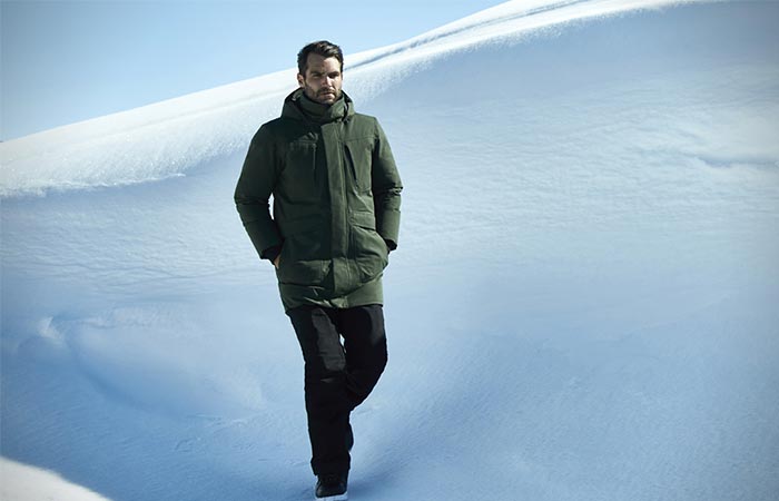 A Guy Walking Down A Snowy Hill Wearing A Green Jacket