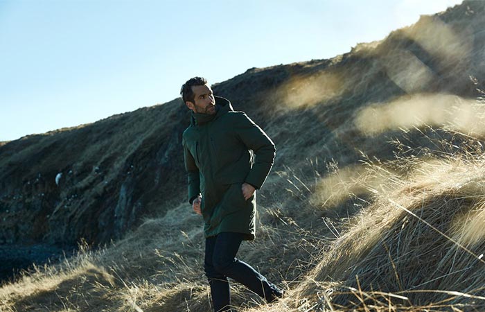 A Guy In Green Aether Apparel’s Tromso Jacket Walking Down The Hill