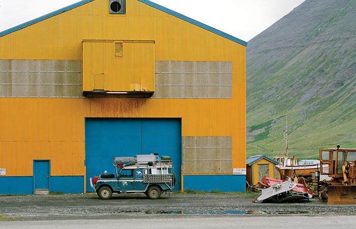 Alloy + Grit Magazine Photo of a Land Rover in front of a blue and yellow shed