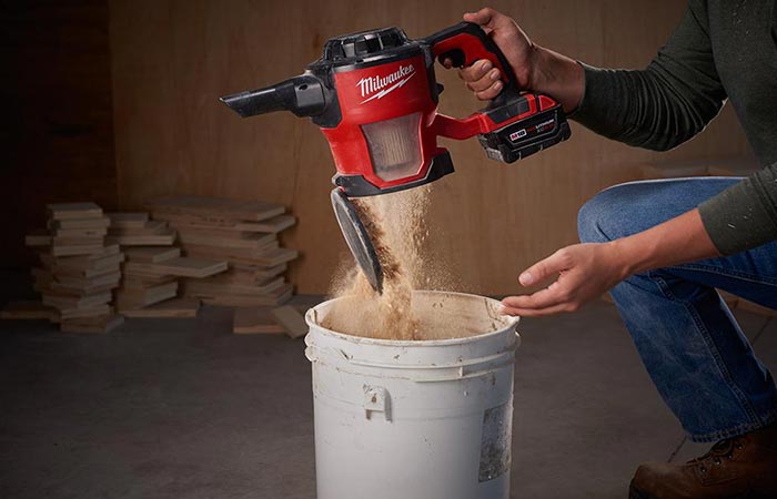 Milwaukee M18 Compact Cordless Vacuum Cleaner being emptied by a man in a workshop
