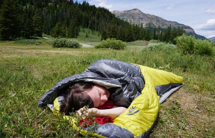 Man using the Sierra Designs Backcountry Elite Sleeping Bag in a mountainous area.