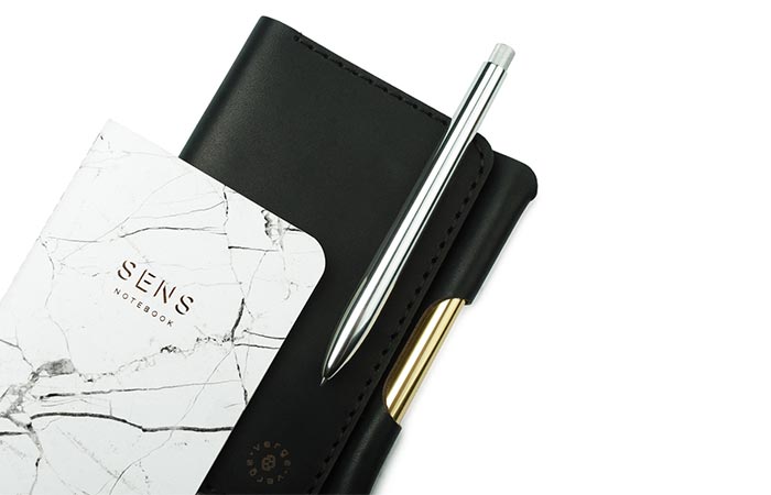 VERGE Pocket Assistant with black leather cover, white marble notebook, and silver SENS pen.